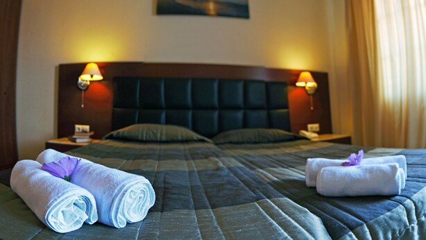 A hotel room with a large bed, two bedside tables, and two wall-mounted lamps. - Belvedere Aeolis Hotel (Lesvos)