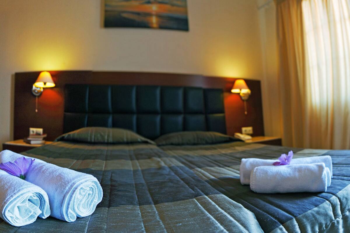 Une chambre d’hôtel avec un grand lit, deux tables de chevet et deux lampes fixées au mur.