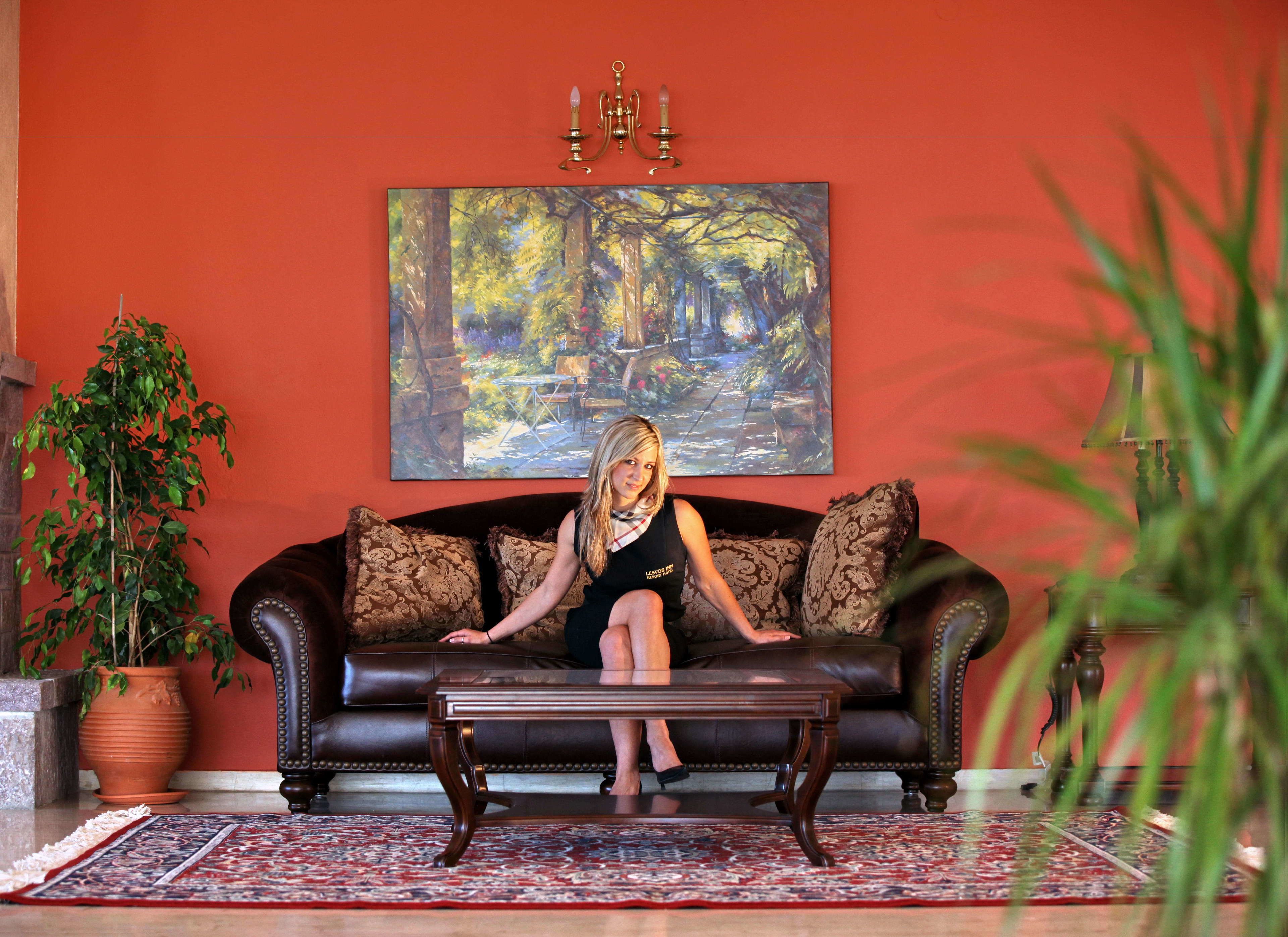 A living room with a dark leather sofa, a coffee table, a large painting on the wall, and a potted plant.