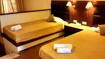 A hotel room with two beds, each with a rolled white towel, a nightstand with a phone, and wall-mounted lamps.