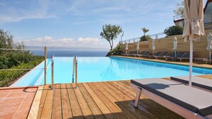 A wooden deck with a pool, lounge chairs, and umbrellas. - Belvedere Aeolis Hotel (Lesvos)