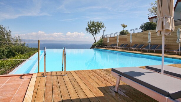 A wooden deck with a pool, lounge chairs, and umbrellas. - Belvedere Aeolis Hotel (Lesvos)