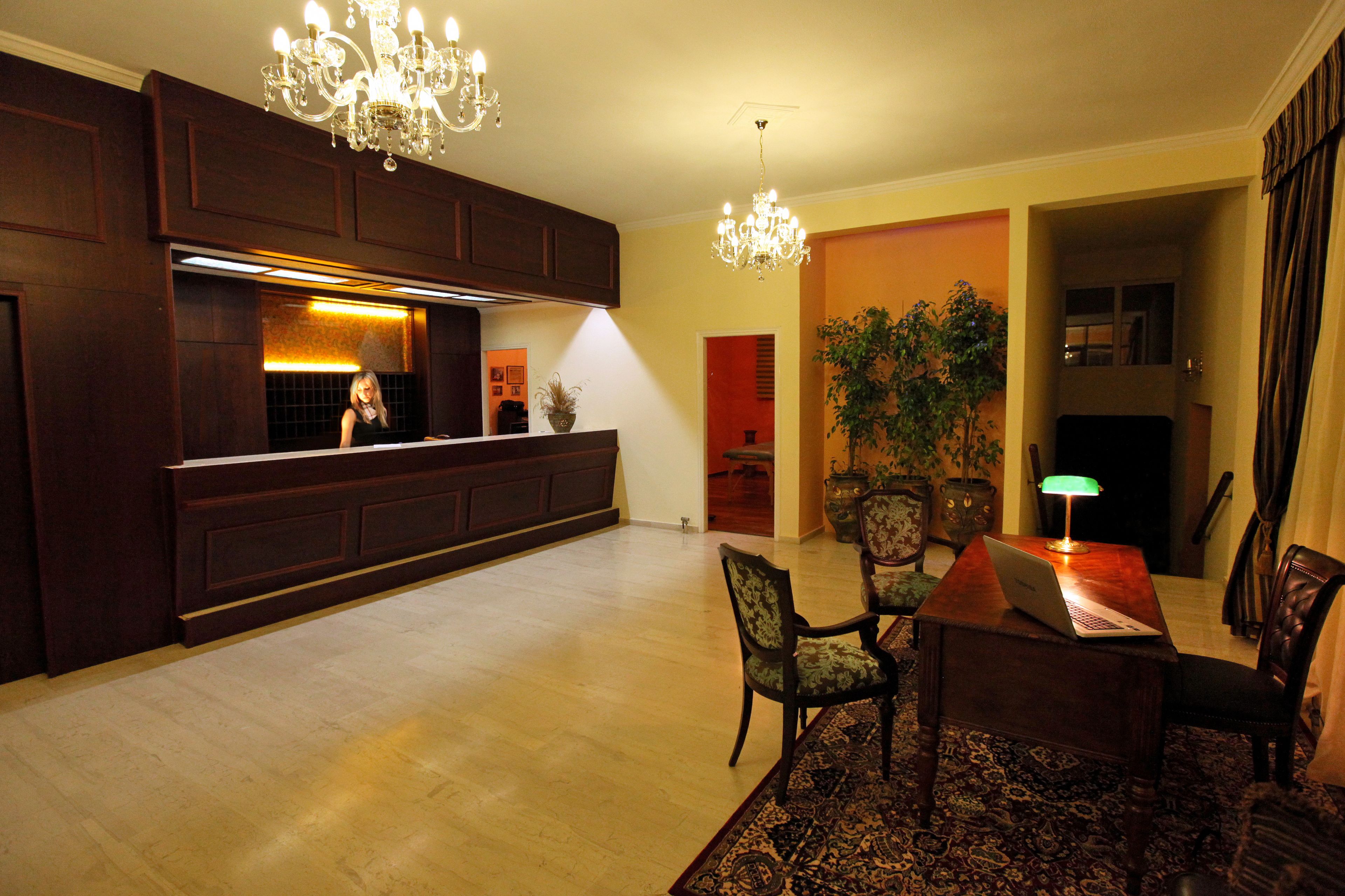 A spacious living area with a wooden floor, a dining table with chairs, a chandelier, and a kitchen area with dark wood cabinets and a countertop.