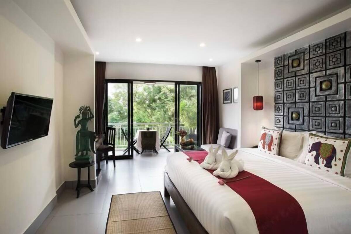 Ein Hotelzimmer mit einem großen Bett, einem Fernseher, einem Balkon mit Tisch und Stühlen sowie einer dekorativen Wand.