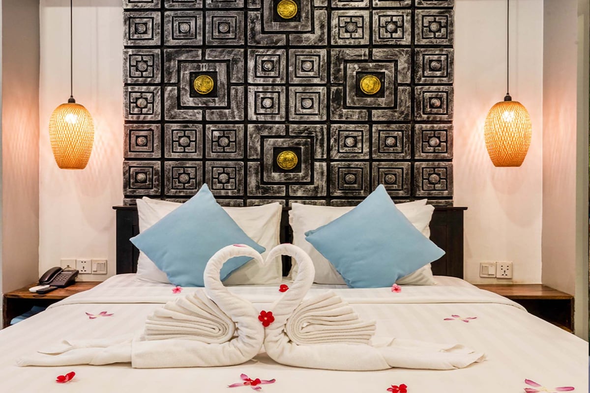 A hotel room with a large bed, two nightstands, a decorative wall, and two hanging lamps.