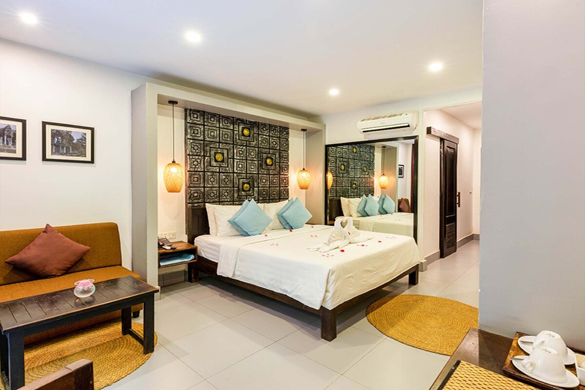 A hotel room with a bed, a sofa, a small table, a mirror, and a wall with a decorative pattern.