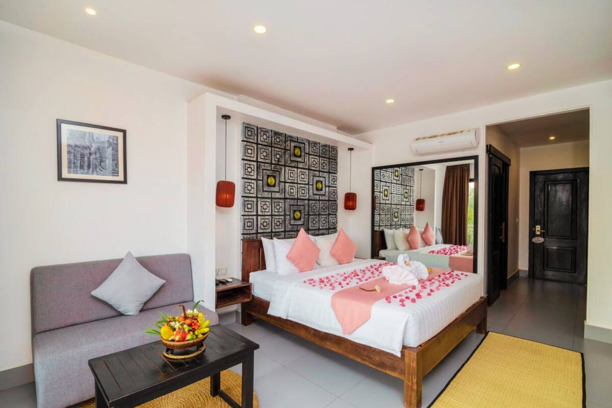 Habitación de hotel con cama, sofá, una mesita con frutero y un muro decorado con motivos.