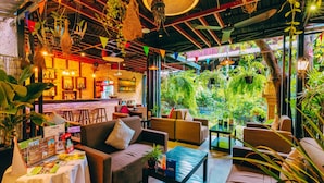 A cozy indoor seating area with sofas and tables, surrounded by lush greenery and hanging plants. - Ladear Privilege Rooms (Siem Reap)