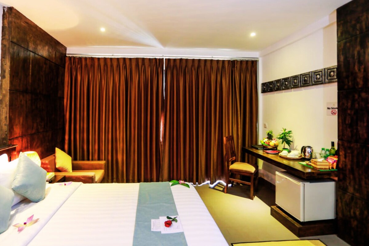 A hotel room with a bed, a desk with a computer, a chair, and a small refrigerator.