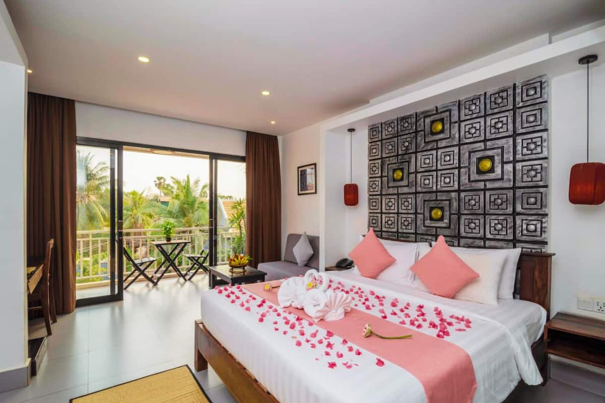Habitación de hotel con cama, balcón, pared con diseño geométrico y vista a palmeras.