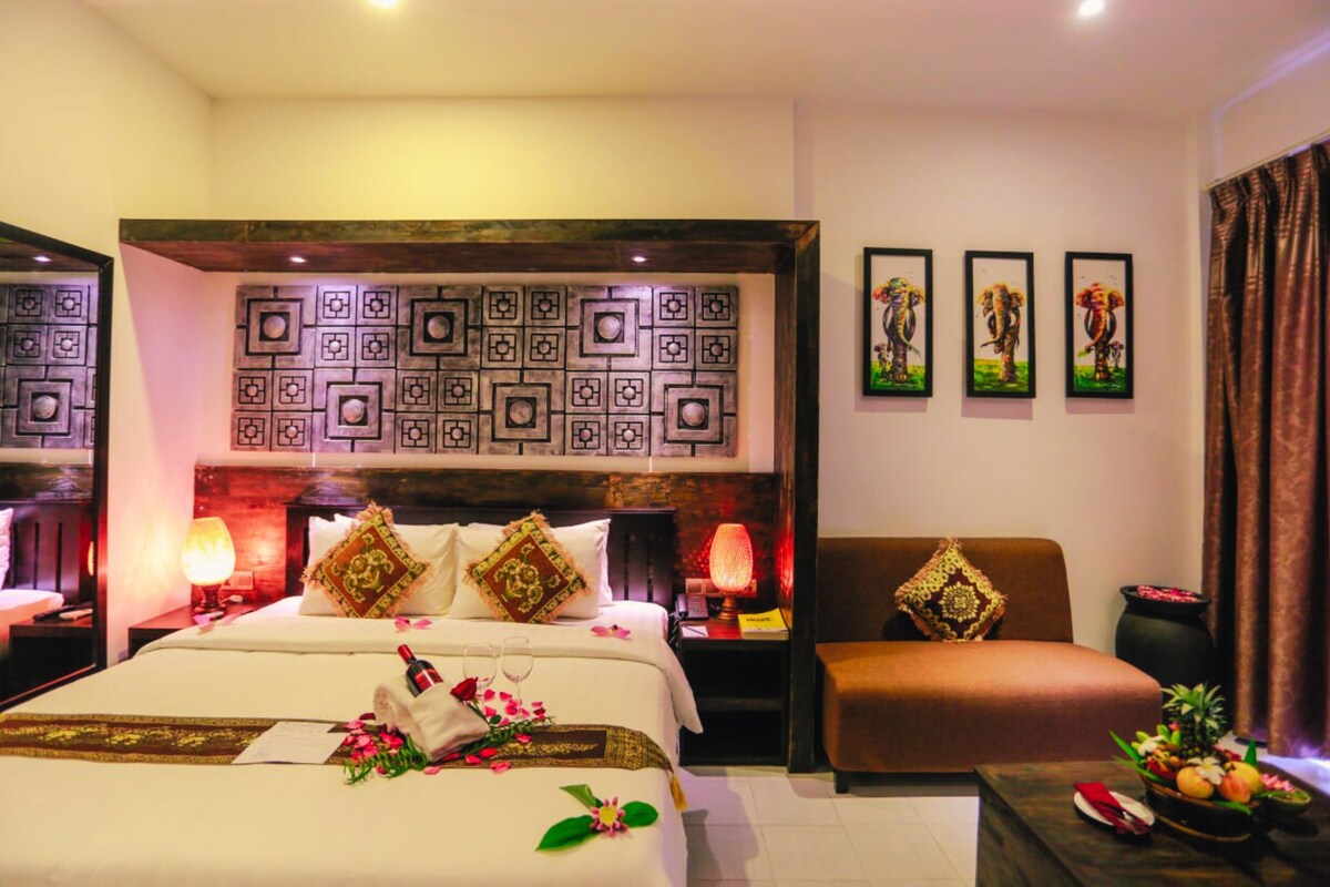 Una habitación de hotel con cama, sofá, mesita de noche, lámpara y cuadros en la pared.