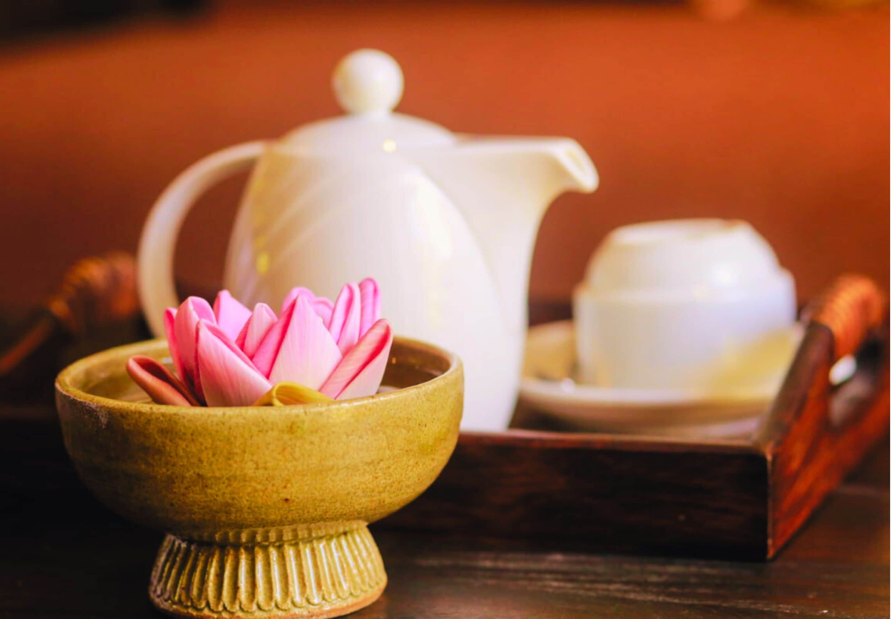 A traditional tea set with a teapot, a cup, and a small bowl containing a pink lotus flower.