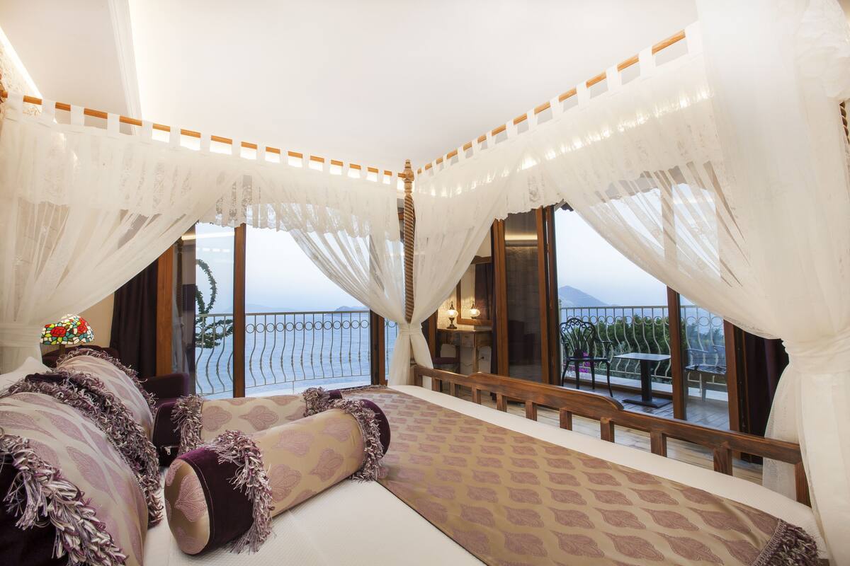 Un dormitorio con una cama grande, cortinas blancas y un balcón con vistas al mar.