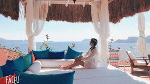 A person relaxing on a white sofa with blue cushions, under a thatched roof, overlooking a scenic view of the sea and mountains. - Hotel Marsala (Kas)