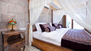 A bedroom with a four-poster canopy bed, a bedside table with a lamp, and a stone wall. - Hotel Marsala (Kas)