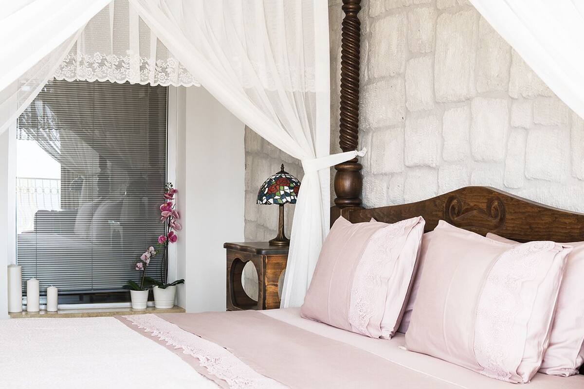 Un dormitorio con cama con dosel, una mesita de noche con lámpara y una orquídea en maceta.