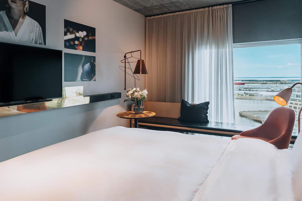 Una camera d'albergo con un letto, una televisione, una finestra vista, una lampada e un vaso con fiori.
