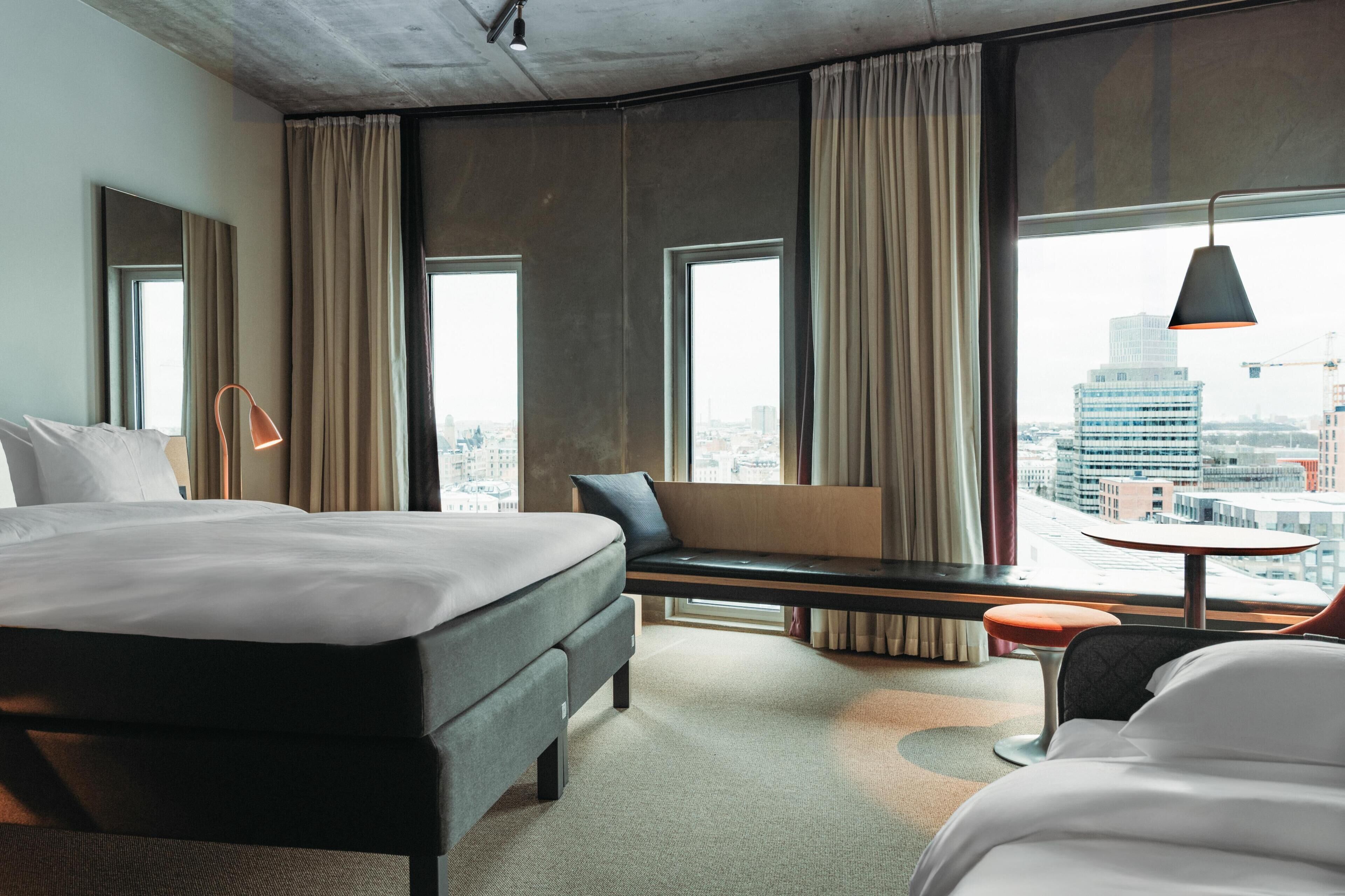 Quarto de hotel com uma cama grande, um banco com vista, uma mesinha e uma cadeira.