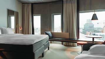Quarto de hotel com uma cama grande, um banco com vista, uma mesinha e uma cadeira.