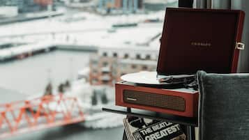 Een Crosley draaitafel op een tafel, met een vinylplaat, een boek getiteld 'The Beatles Greatest Hits', en op de achtergrond een rivier met gebouwen en een brug.