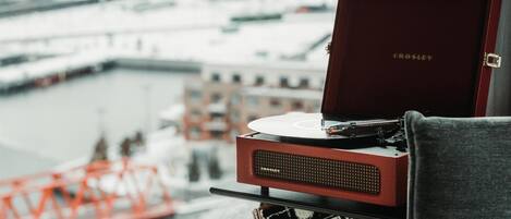 Un tocadiscos Crosley sobre una mesa con un disco de vinilo, un libro titulado 'The Beatles Greatest Hits', y una vista de un río con edificios y un puente al fondo.