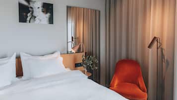 A hotel room with a bed, a chair, a mirror, and a window with curtains.
