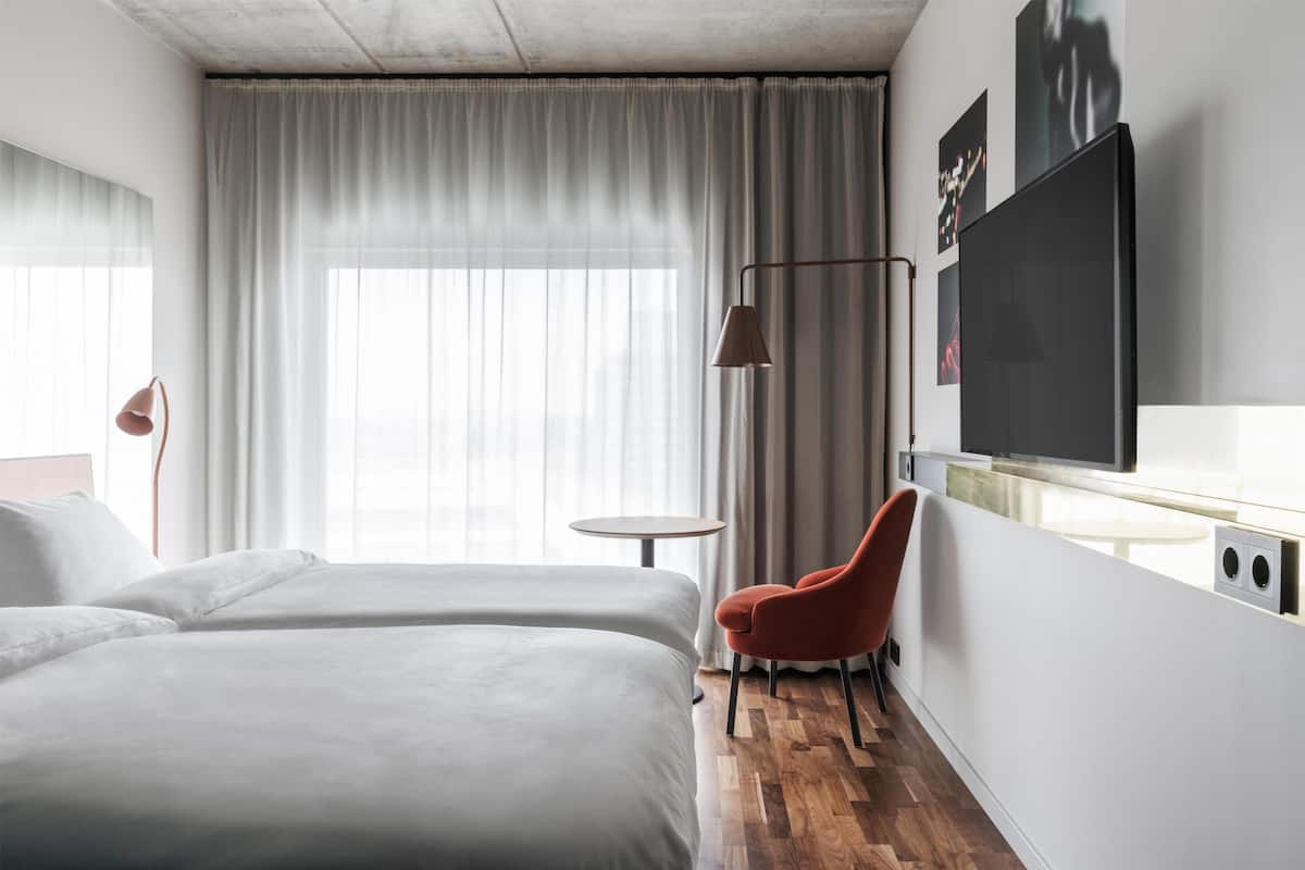 Una camera d'albergo con un letto, una sedia, una televisione e una finestra con tende.