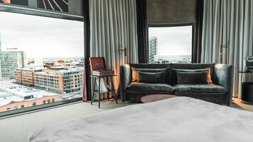 A hotel room with a large bed, a sofa, a chair, and a view of the cityscape.