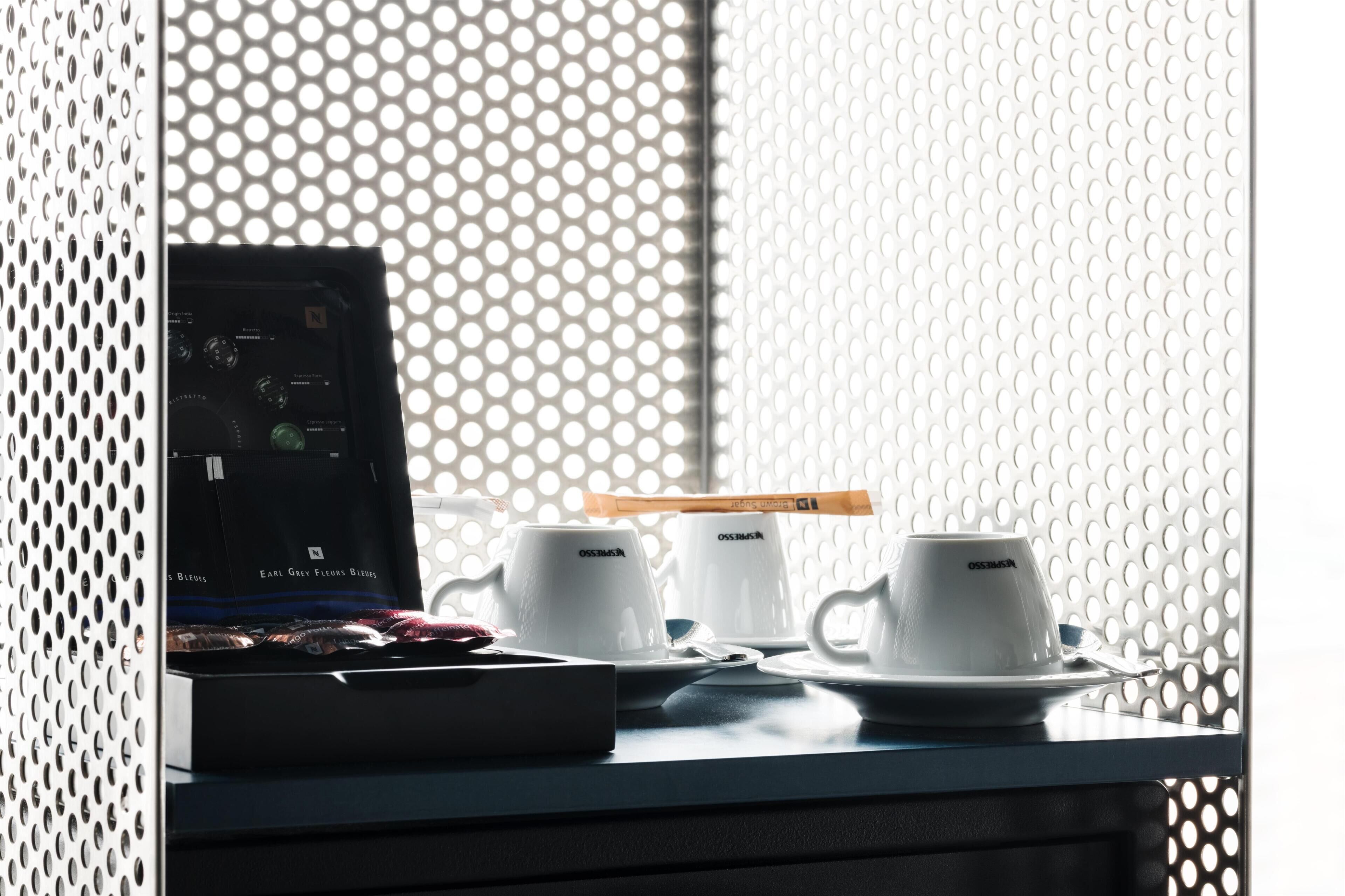 A table with a laptop, two white cups, a spoon, and a tray with a box of tissues.