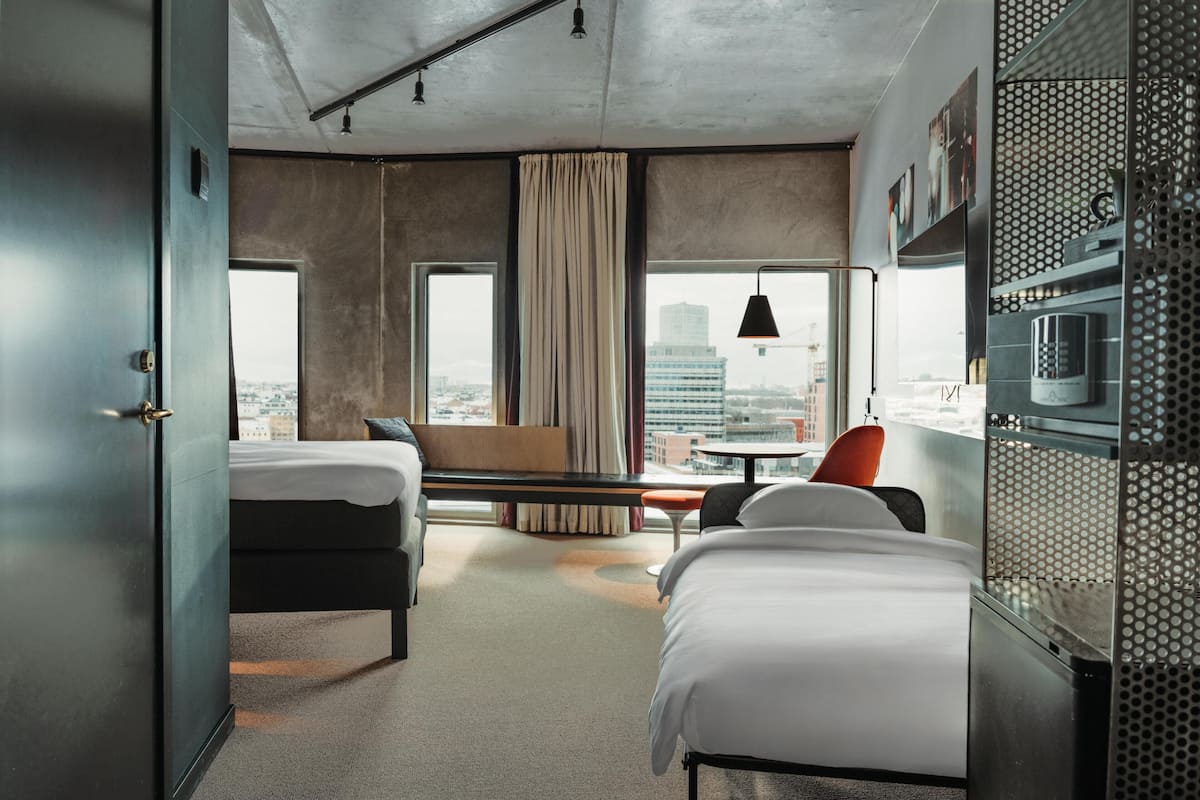 Una camera d'hotel con un letto, una scrivania, una sedia, una finestra vista città e angolo cottura.