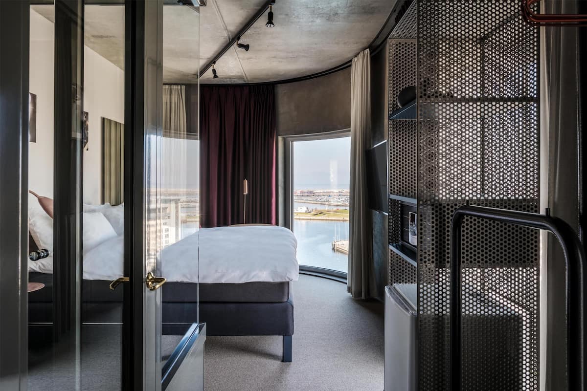 Una camera d'albergo moderna con un letto, vista sulla città e un balcone con ringhiera.
