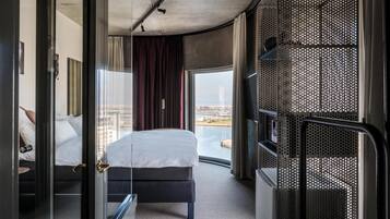 Ein modernes Hotelzimmer mit Bett, Blick auf die Stadt und einem Balkon mit Geländer.
