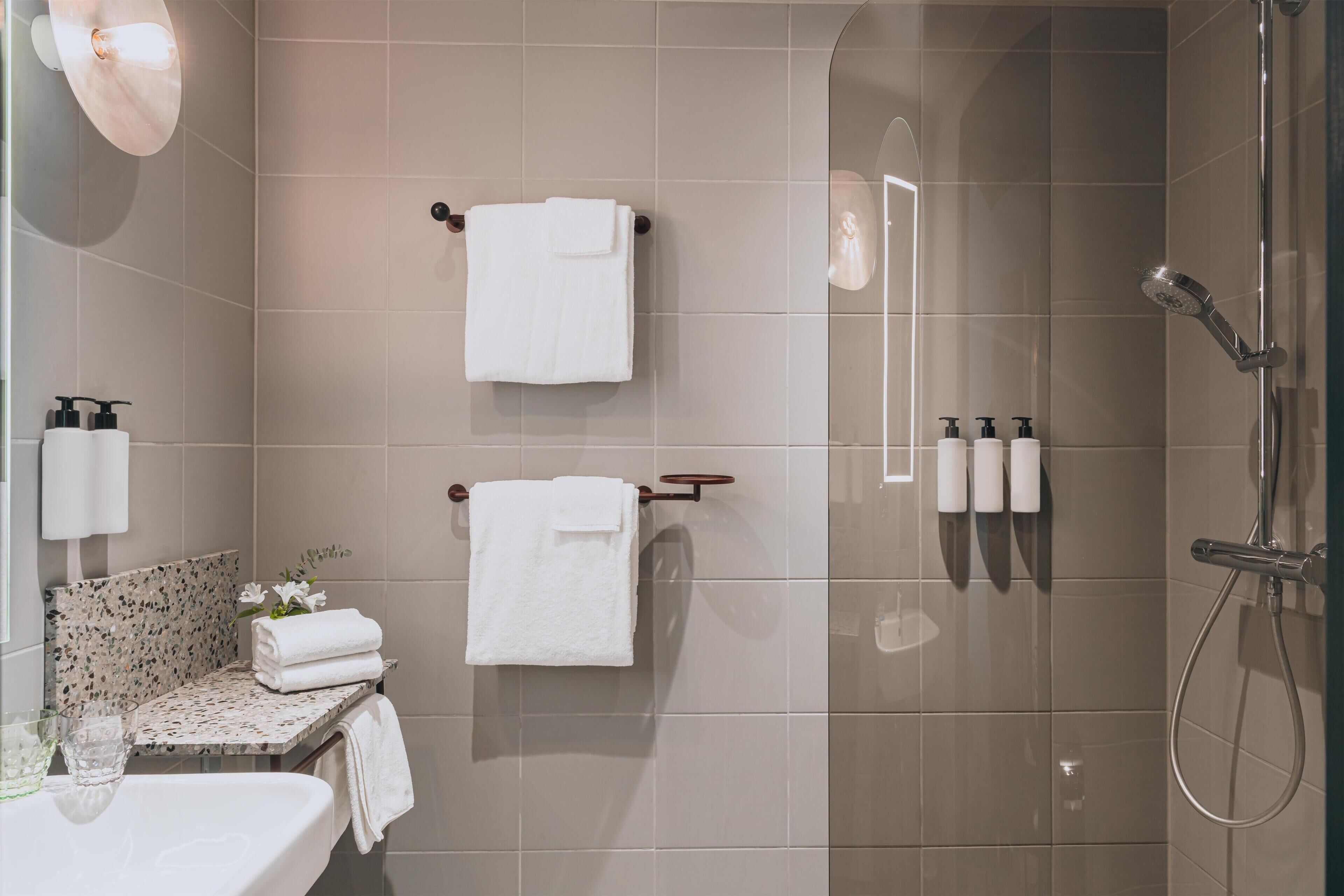 Un baño moderno con ducha compartimentada con vidrio, dos barras para toallas, un lavamanos con artículos de tocador y un salpicadero decorativo de azulejos.