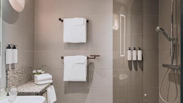 Un baño moderno con ducha compartimentada con vidrio, dos barras para toallas, un lavamanos con artículos de tocador y un salpicadero decorativo de azulejos.