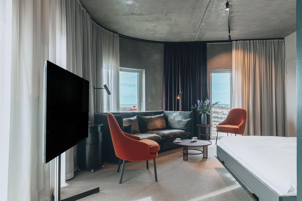 Una camera d'albergo moderna con televisione a schermo piatto, un divano, un letto singolo, un tavolino da caffè e una sedia.