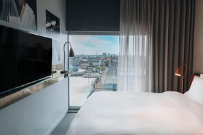 A hotel room with a large bed, a TV, a city view, and a window with curtains. - STORY HOTEL MALMO, in JdV by Hyatt (Malmö)