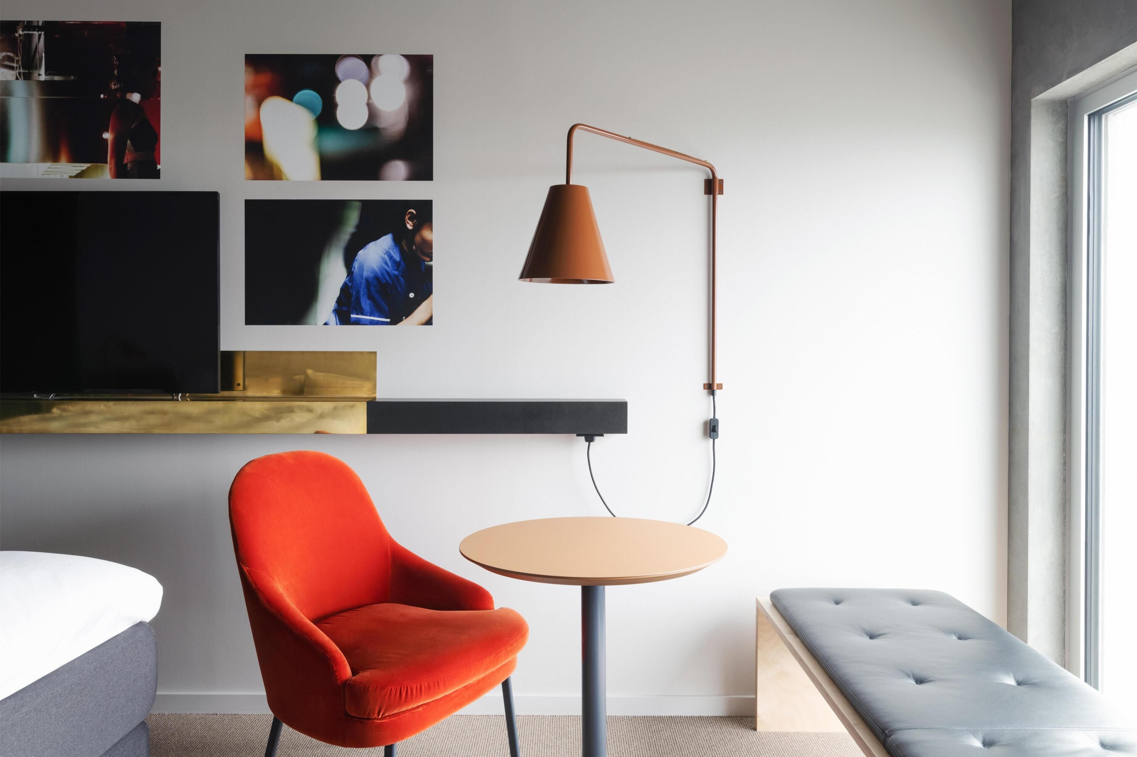 A modern room with a red chair, a round table, a floor lamp, a TV, and artwork on the wall.
