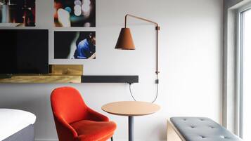 A modern room with a red chair, a round table, a floor lamp, a TV, and artwork on the wall.