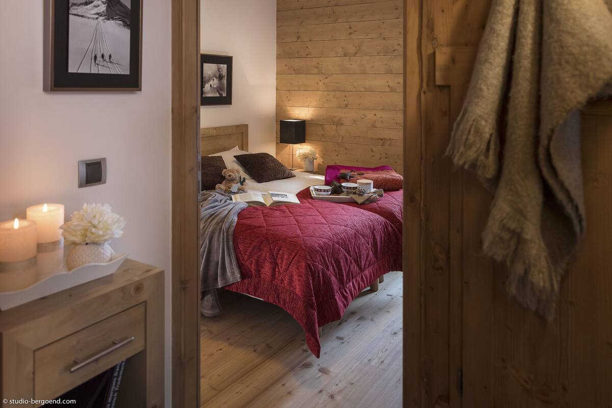 A bedroom with a wooden headboard, a bed with a red blanket, a bedside table with candles, and a framed picture on the wall.