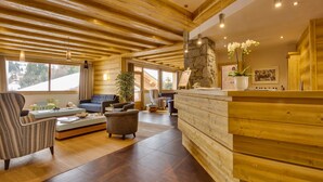 A spacious living area with a wooden ceiling, a stone accent wall, and a reception desk. - CGH Residence Boutique les Chalets de Léana (Araches-la-Frasse)