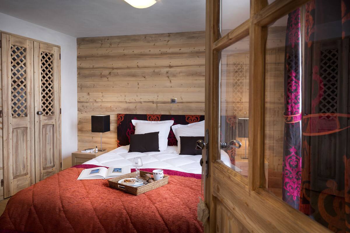 A bedroom with a wooden headboard, a bed with white and black bedding, a bedside table with a lamp, and a tray with breakfast items.