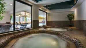A spa area with two hot tubs, large windows, and a view of an outdoor pool area. - CGH Residence Boutique les Chalets de Léana (Araches-la-Frasse)