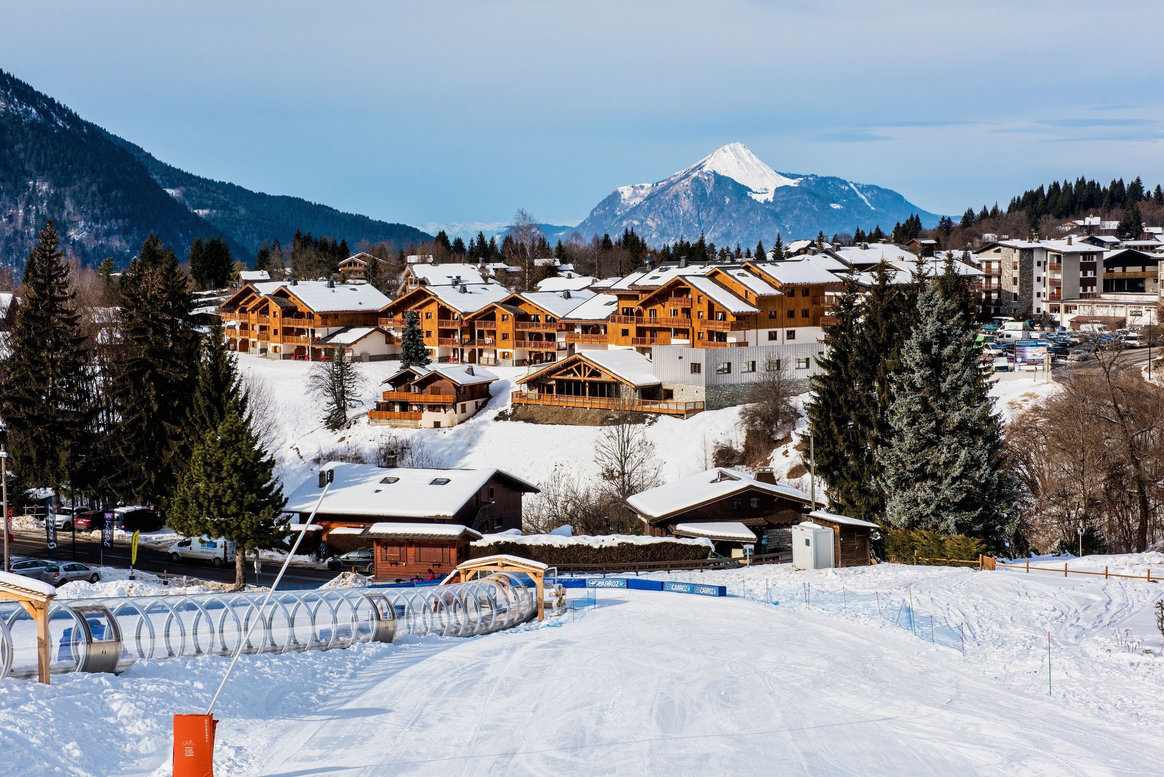 A ski resort with wooden lodges, a snow-covered mountain, and a clear sky.