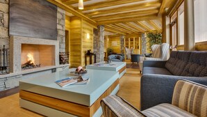 A cozy living room with a stone fireplace, wooden beams, and comfortable seating. - CGH Residence Boutique les Chalets de Léana (Araches-la-Frasse)