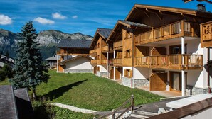 A wooden chalet with balconies, set against a mountainous backdrop. - CGH Residence Boutique les Chalets de Léana (Araches-la-Frasse)
