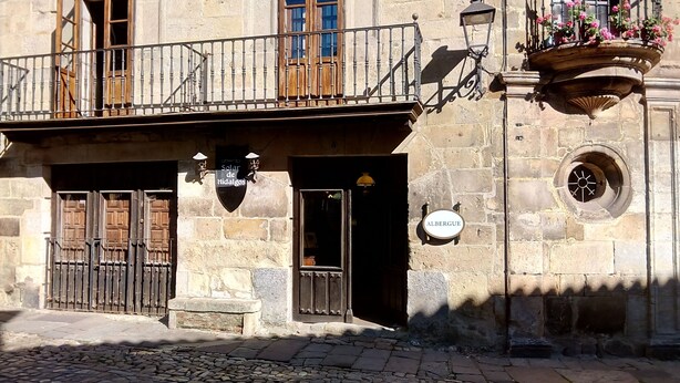 Un bâtiment en pierre doté d’un balcon, d’une porte avec une enseigne et d’une fenêtre ornée d’un panier de fleurs.