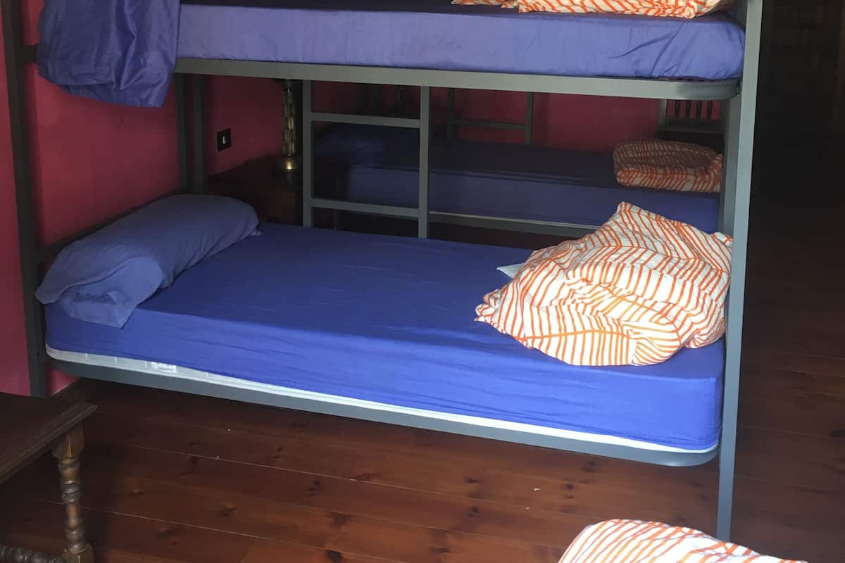 Un lit superposé à deux niveaux, chaque niveau étant doté d’un matelas bleu et d’oreillers à rayures orange. Un lustre est suspendu au-dessus du lit, et le sol est en bois.