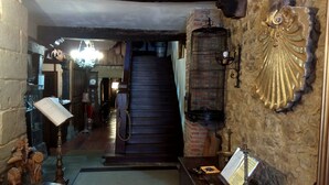 Un couloir étroit avec un escalier en bois menant à un deuxième étage. Une cage à oiseaux, sur laquelle est fixée une lampe, est suspendue au mur.