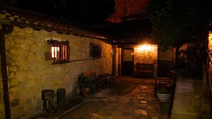Un bâtiment en pierre avec un banc en bois et une petite table, un chemin en pierre et une lanterne allumée.