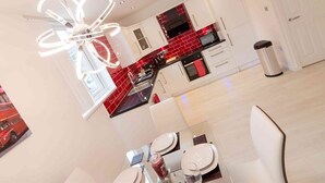 Een moderne keuken met witte kastjes, een rode spatwand, en een eethoek met een witte tafel en stoelen.